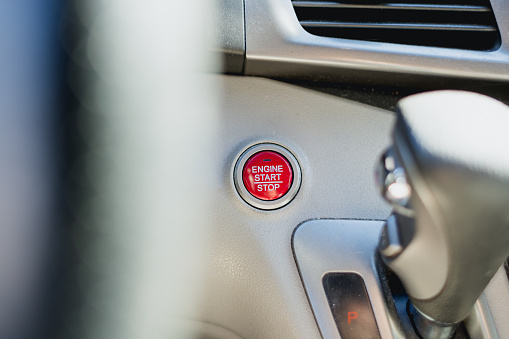 A modern car with a push button engine start stop button. The button stands out as it is vibrant red color.