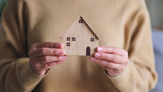 Closeup image of a woman holding and showing a wooden house model