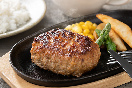 Juicy hamburger steak grilled on a steaming iron plate