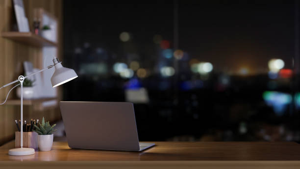 istock A laptop computer, a table lamp, and decor on a desk near the window with a nighttime view. 2092949278