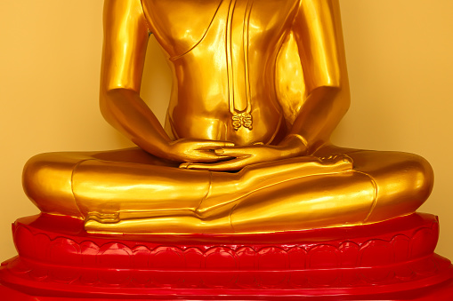 Close up shot of a golden Buddha sitting in Lotus position (Padmasana) statue as part of a local landmark monument and place of worship in a clear blue sky