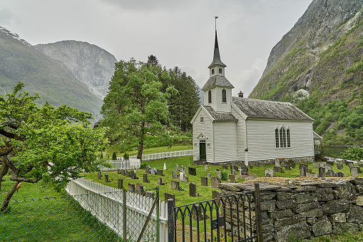 traditional old fashioned white wooden stave church in the beautiful and tranquil landscape at the Naeroyfjord in Norway with snow covered mountains in the background.
