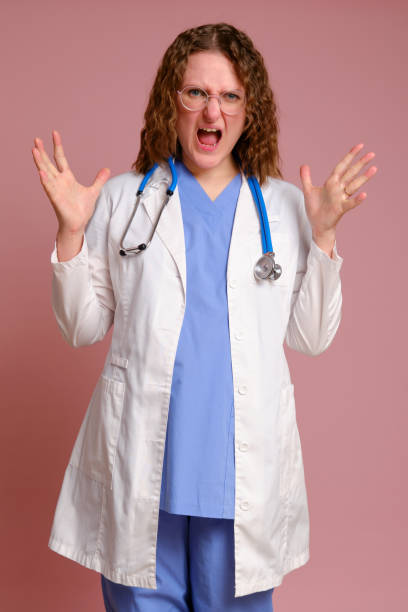 яростно кричащая женщина-доктор, студия розового фона. медсестра в униформе со стетоскопом на красном студийном фоне - furiously стоковые фото и изображения