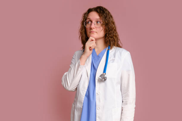 pensive woman doctor, studio pink background. nurse in uniform with stethoscope on red studio background - doctor thinking asking pensive fotografías e imágenes de stock