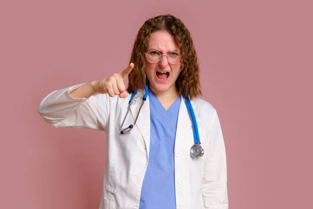 furiously screaming female doctor, studio pink background. nurse in uniform with stethoscope on red studio background - furiously photos et images de collection