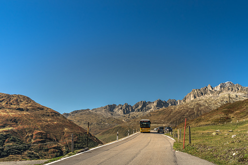 Realp, Canton of Uri, Switzerland - September 26, 2023. Mountain landscape at the Furka Pass, a yellow public bus drives on the pass road