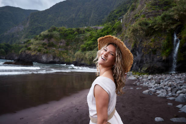 Portrait of carefree woman with straw hat standing on the beach and looking at camera. Copy space.