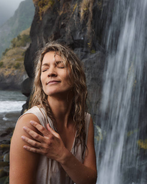 Young woman standing with her eyes closed by the waterfall during the day on the beach.