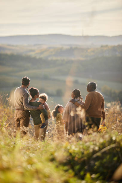 Back view of happy black extended family talking in autumn day on a hill. Rear view of happy African American multi-generation family communicating while spending an autumn day on a hill. Copy space. multi generation family stock pictures, royalty-free photos & images