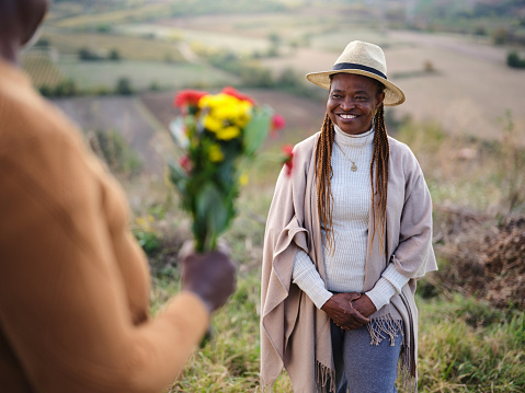 Happy African American senior woman enjoying while receiving flowers from her husband on a hill. Photographed in medium format.