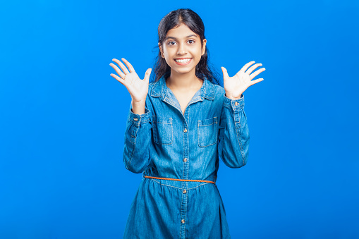 Portrait of an excited lovely Indian girl showing open palm of hand having ten fingers with happy face expression