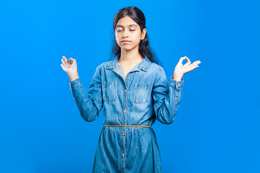 a beautiful Indian girl showing Gyan Mudra with closed eyes on blue background