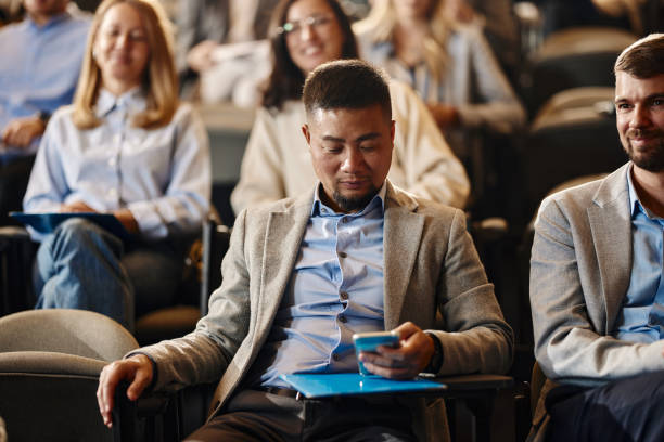 istock Young Chinese businessman using cell phone on a seminar in convention center. 2093313333