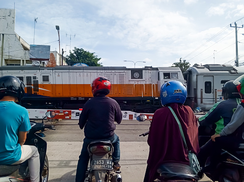 pekalongan, central java, indonesia - march 16 2024. Motorbike riders stop at railway crossings when a train passes