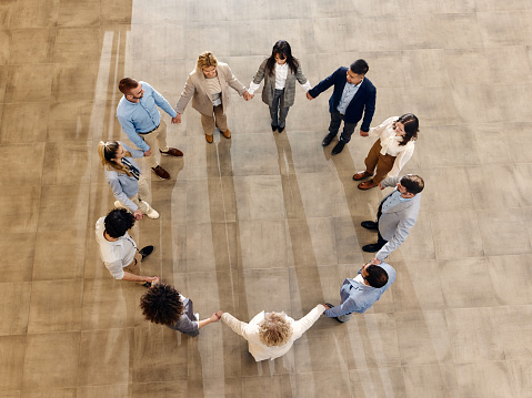 High angle view of team of happy entrepreneurs holding hands while standing in a circle at hallway. Copy space.