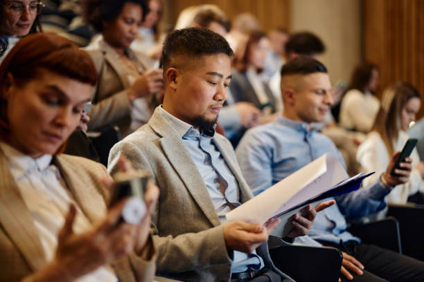 istock Asian businessman going through paperwork on a seminar in convention center. 2093326349