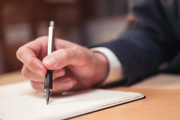Closeup of male hand with pen businessman writing notes and remarks in notebook, selective focus