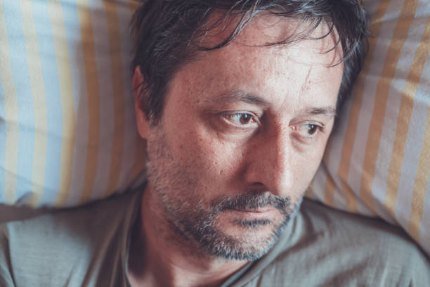 Sad man sitting on a side of the bed, leaning on his hands