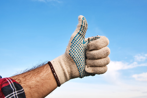 Gardener wearing gardening gloves gesturing thumbs up as a recommendation and approval hand sign, selective focus