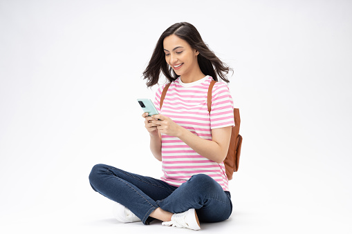 Full length body size photo of young girl using phone sitting on floor wearing jeans denim t-shirt footwear isolated over white background