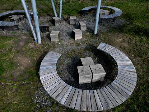 three round benches in the park. the grill is in the middle of sitting. large wood-paneled crescent moon in a meadow under a pergola. massive wooden blocks