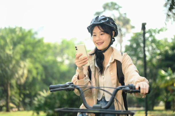istock Happy smiling young woman in safety helmet using mobile phone while sitting on a bicycle 2093404552