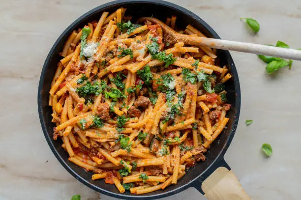 Simple and easy pasta pan with macaroni, minced meat, tomatoes, herbs and parmesan cheese. Served hot and ready to eat in a skillet isolated on kitchen counter background. Closeup