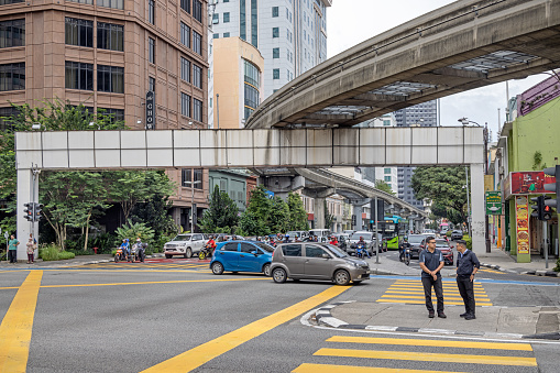 Kuala Lumpur, Malaysia - January 9th 2024:  Two men in a zebra crossing in front of the traffic under the famous monorail track in the Malaysian capital