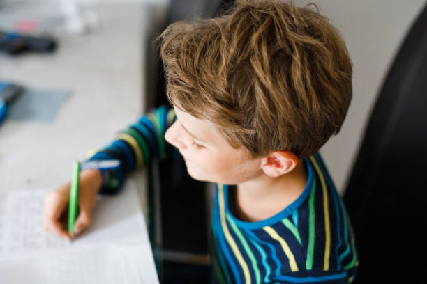 istock Hard-working happy school kid boy making homework during quarantine time from corona pandemic disease. Healthy child writing with pen, staying at home. Homeschooling concept 2093450682