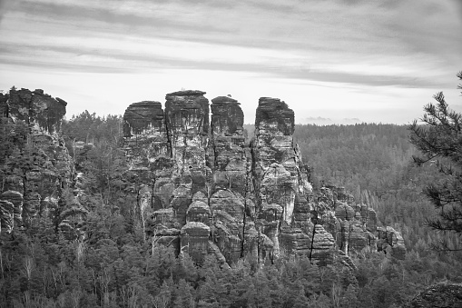 Jagged rocks on the Basteibridge in black and white. Wide view over trees and mountains. National park in Germany