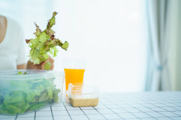 Unrecognizable Asian woman enjoy eating a vegetable salad and drinking an orange juice in the morning, woman eating a vegetable salad in tupperware or plastic box.