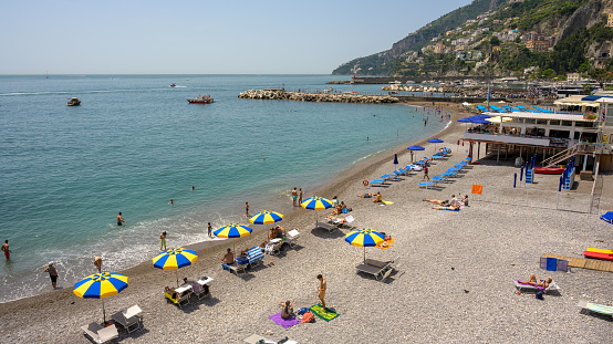 View of the  Mediterranean beach in the picturesque village of Amalfi, Italy, beach restaurants and tourists on the sand.