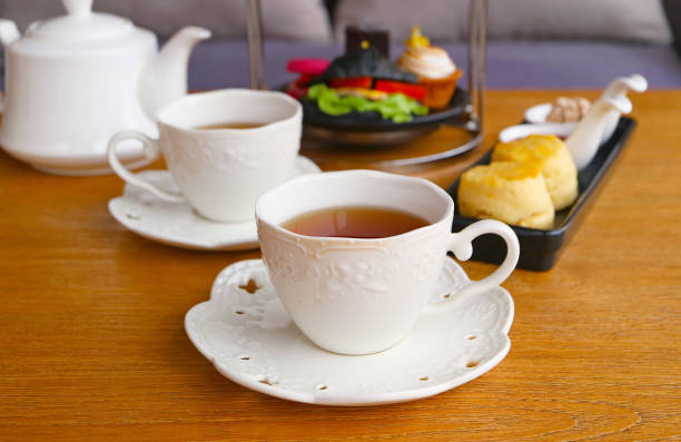 Two Cups of Hot Tea with Blurry Scones and Afternoon Tea Pastries the Backdrop