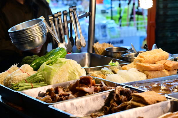 At a stall in Nanjichang Night Market, this close-up shows various vegetables like cabbage, green peppers, and string beans, along with enoki mushrooms. Various ingredients include tofu and vermicelli.