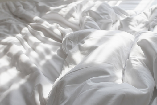 Unmade bed with shades of sunlight through the curtain in morning.