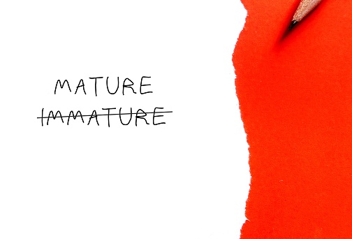 Note paper on orange background with handwritten text cross off IMMATURE to MATURE, means to improve from being person who thinks and acts like child to be immature, think and act like adult