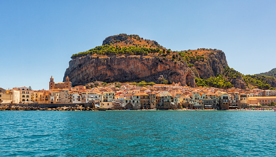 Panoramic view of Cefalù, Metropolitan City of Palermo, coastal town in northern Sicily, Italy.  Old buidings, the Duomo, a Norman Cathedral and La Rocca, a huge rocky mountain, summer time, august 2023.