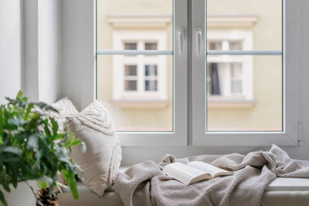 istock Windowsill with decorative cushions, soft plaid and open book in cozy apartment 2093609990