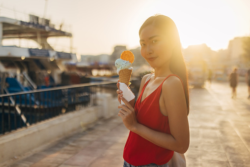 An exotic Asian woman walks around the city and eats her favorite ice cream in a cone