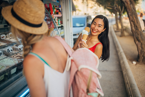 Portrait of a smiling Taiwanese woman looking directly into the camera with a wide smile while her friend chooses an ice cream flavor