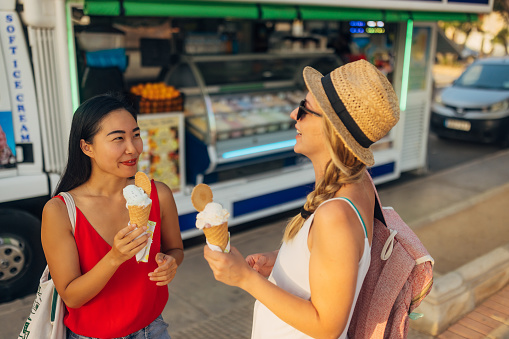 A Taiwanese woman and a white woman eat ice cream in a cone on a summer day and enjoy the refreshment