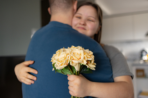 Close up of a woman with special needs embracing her boyfriend after receiving flowers at home.