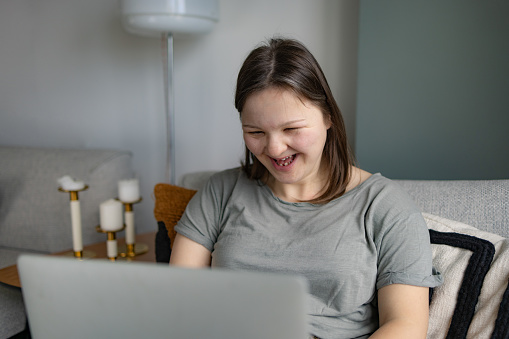 Cheerful woman with Down syndrome having fun while surfing the Internet on a computer in the living room.