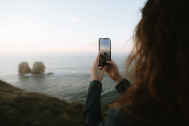 A young woman taking a picture of the sea at sunset with a smart phone