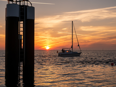 Sailboat on Wadden Sea leaving harbour of Hoernum at sunrise, Sylt island, North Frisia, Schleswig-Holstein, Germany