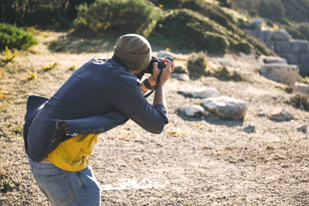 A woman is holding a camera with a strap around her neck. She is wearing a black sweater and has her hands on the camera. Concept of adventure and exploration