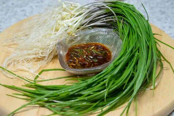 Dalrae seasoning sauce and fresh Wild Chive vegetables on a round wooden base. Dalrae seasoning sauce made with wild chives as the main ingredient, which Koreans enjoy eating in spring.