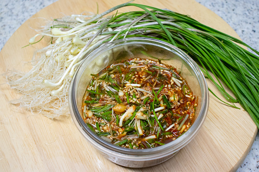 Dalrae seasoning sauce and fresh Wild Chive vegetables on a round wooden base. Dalrae seasoning sauce made with wild chives as the main ingredient, which Koreans enjoy eating in spring.