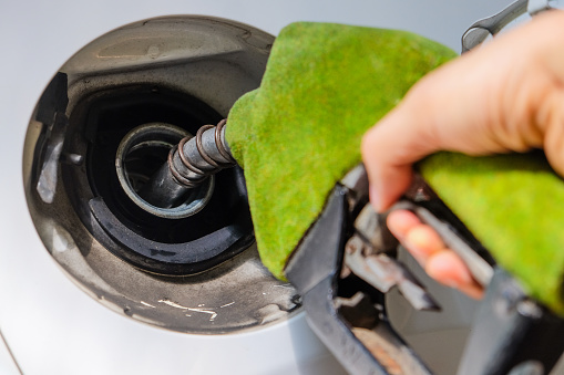 Close up image of hand refilling a car with fuel at a gas station, green fuel nozzle,energy concept