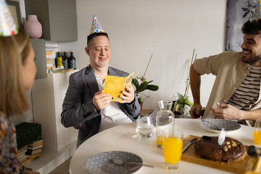Happy man with Down syndrome reading a Birthday card while having a party with his friends at home.